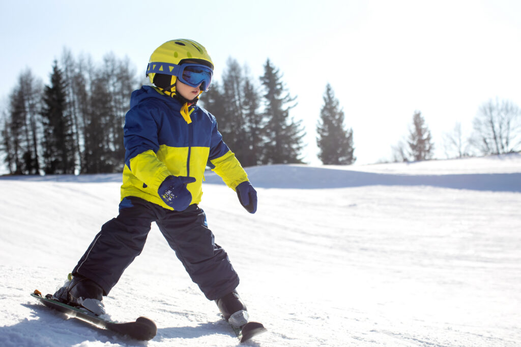 Cute toddler child in colorful ski wear, skiing in Italy on a sunny day, kids and adults skiing together